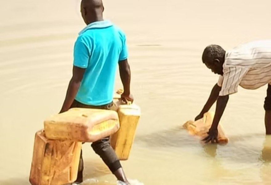 Two men fill yellow jerrycans from a muddy river