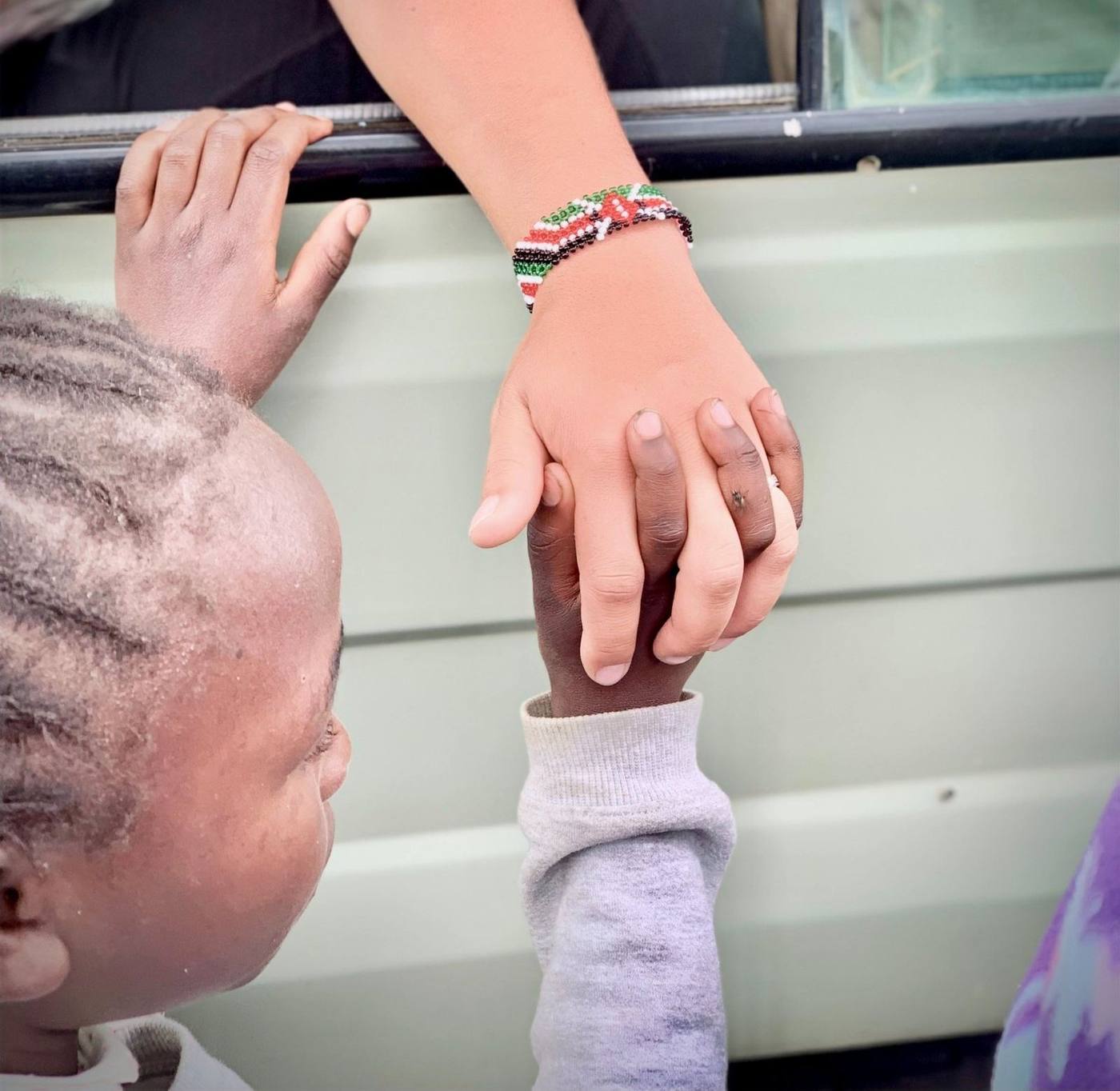 A volunteer's hand holds a child's hand through a vehicle window