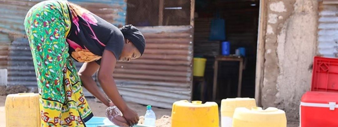 A woman washing dishes beside yellow jerrycans
